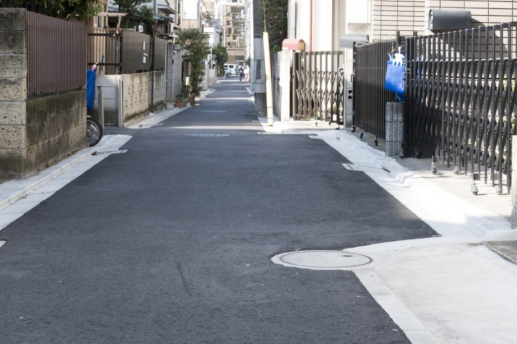 住宅の塀や門に挟まれた道幅の狭い住宅街の道路