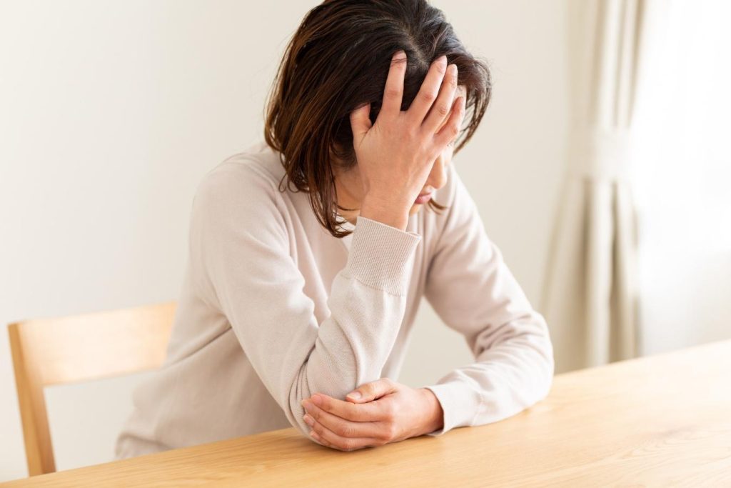 ダイニングテーブルで額に手を当てて考え込む女性
