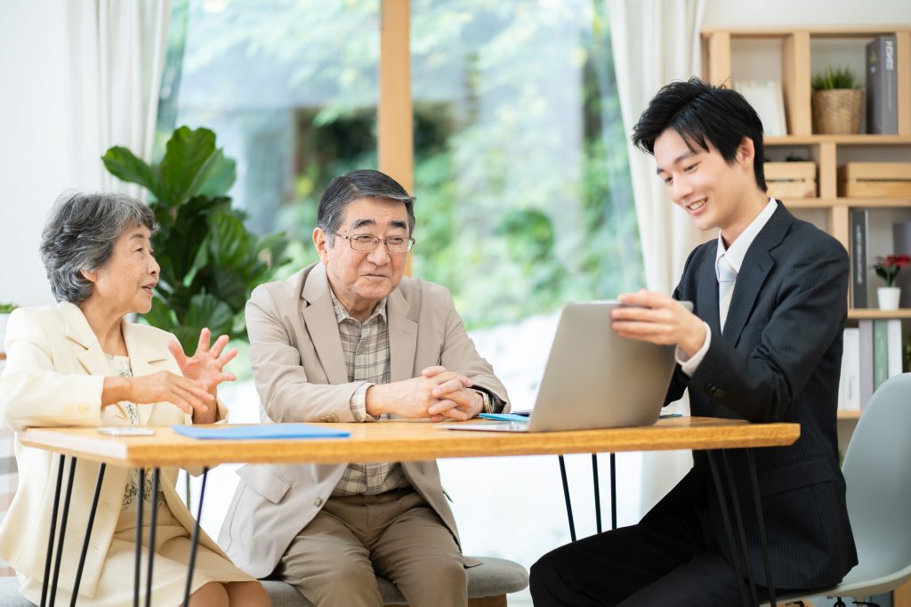 スーツを着た専門スタッフがノートパソコンを見せながら高齢夫婦に説明・相談をしている様子