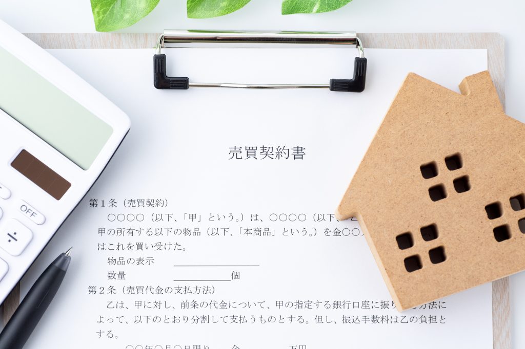 「売買契約書」と書かれた書類と、その上に置かれた木製の家型プレート