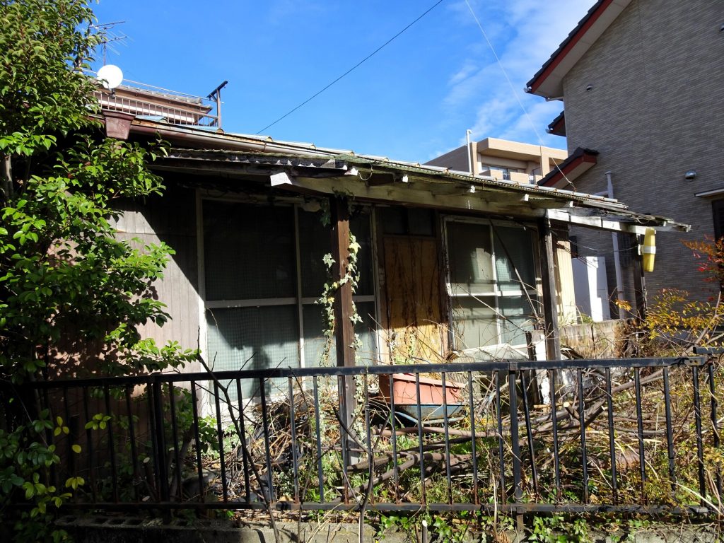 庭木や雑草に囲まれた古い木造住宅の外観