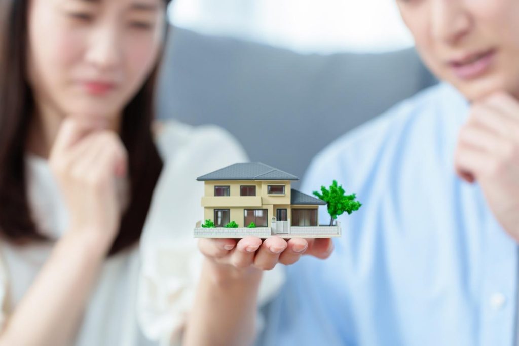 家の模型を手のひらに乗せて悩む夫婦