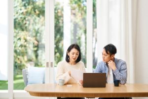紙の書類を見ながら調べものをする夫婦。