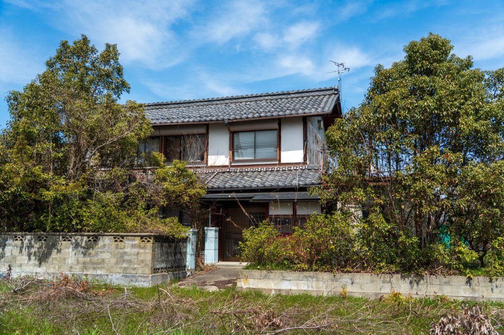青空のもとに建つ、瓦屋根の和風一戸建て空き家の外観