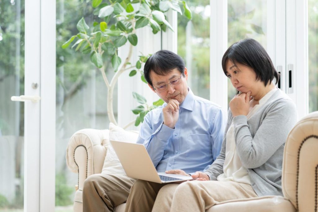 ノートパソコンを見ながら考え事をする夫婦。