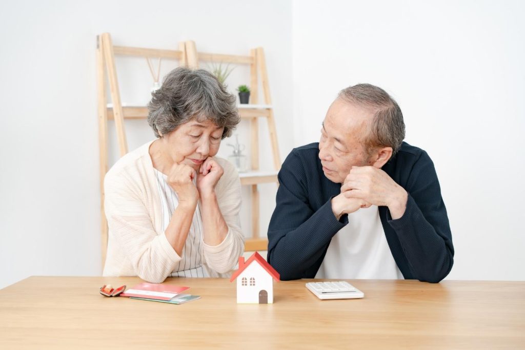 住宅模型や電卓が置かれたテーブルの前で悩むシニア夫婦