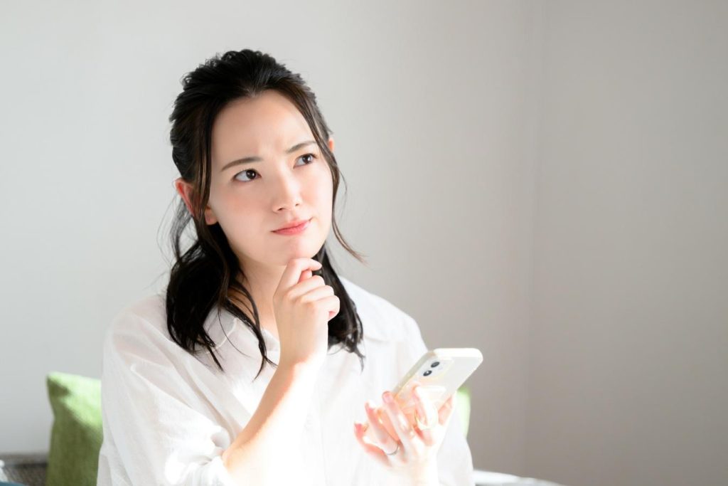 スマートフォンを手に持ち首をかしげる女性