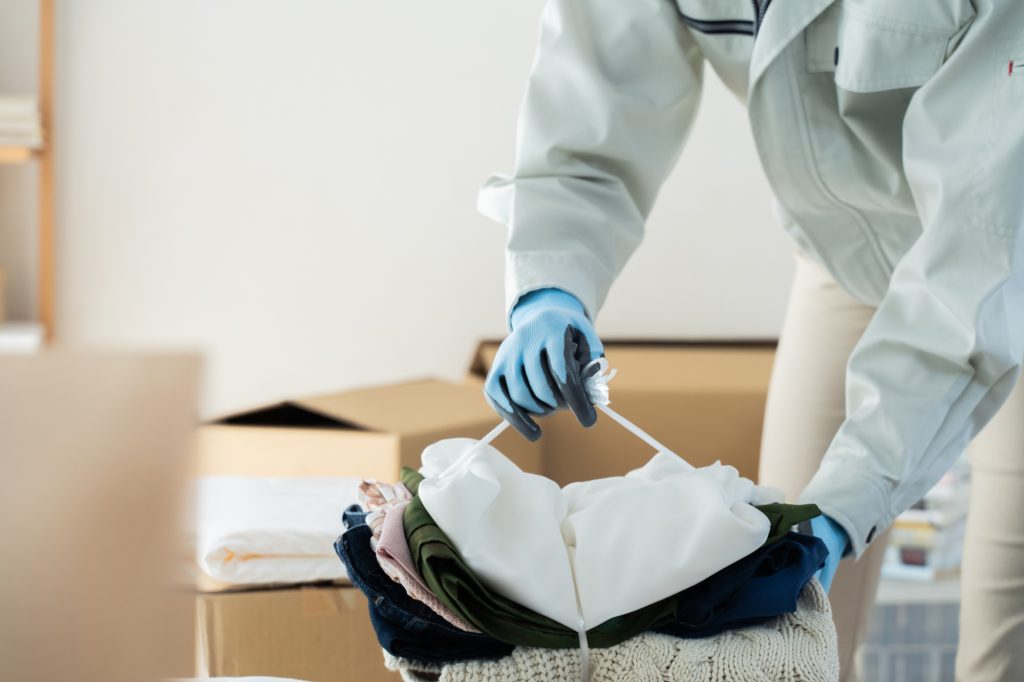 作業服と手袋を着用した整理業者が、段ボール箱の上で不用品・衣服を紐で丁寧に縛って梱包している様子