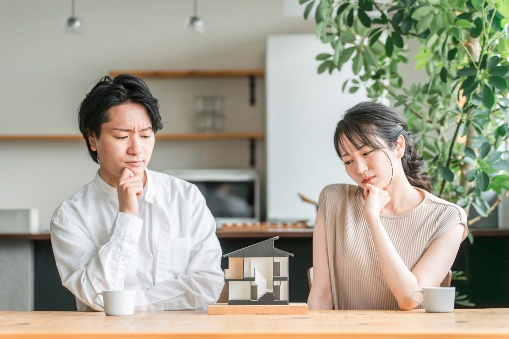 顎に手を当てて、難しい顔で家の模型を見る夫婦