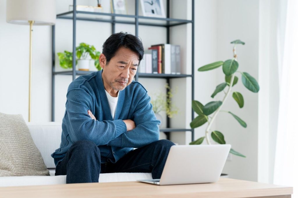 自宅のソファに座り、難しい顔で腕組みをしてパソコンを眺める男性