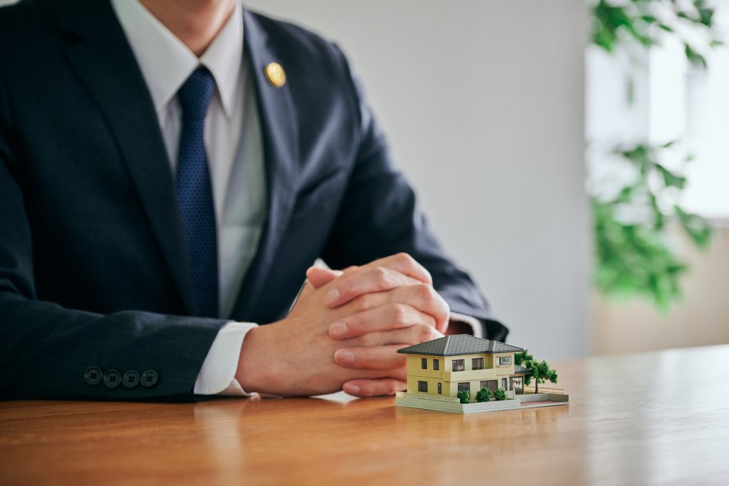 スーツを着た専門家がテーブルに住宅模型を置き、空き家の整理や相続・活用について相談に応じている様子